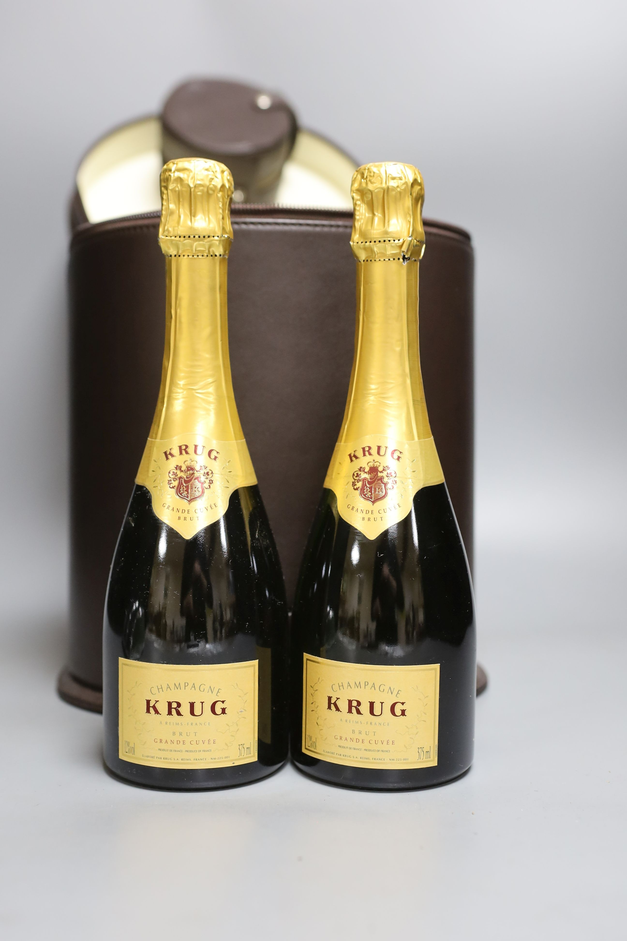 A Connolly leather Krug champagne carrier with dust cover, containing: two half bottles, two champagne chillers, two Krug champagne flutes, two Connolly linen napkins, a leather caviar pouch and two bone caviar spoons